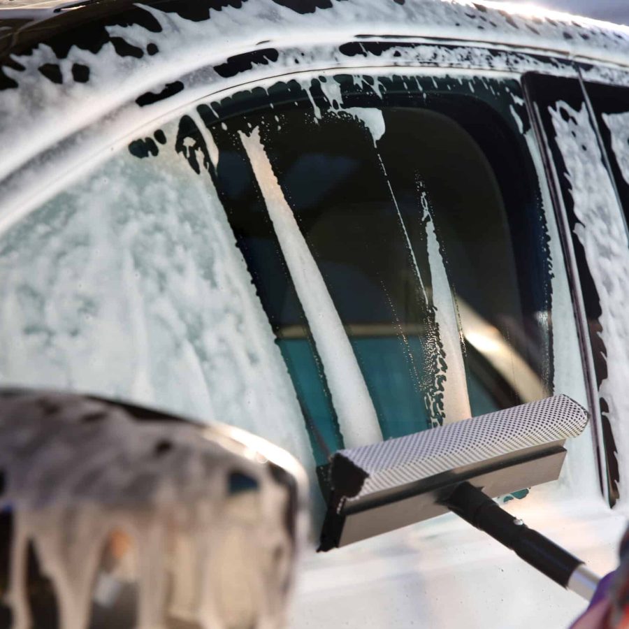 Worker cleaning automobile window with squeegee at car wash, closeup